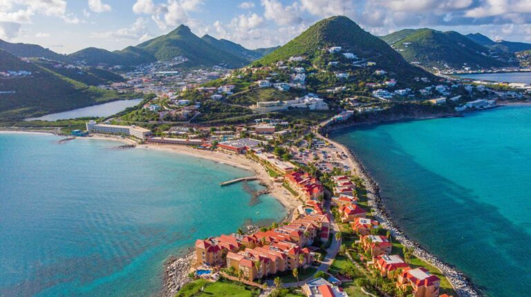 High Aerial view of the caribbean island of St. Maarten, with building along the anrrow stripsof land, mountain peaks in the distance and green-blue sea along the coast.