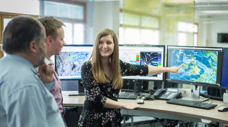 Woman looking at weather map on computer screen with two colleagues.
