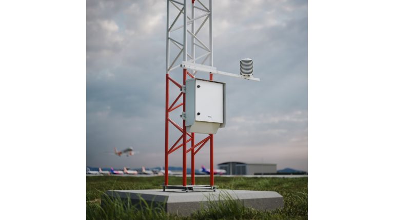The Vaisala AWS810 Airport Edition automatic weather station in operation at an airport, with aircraft taxiiing along the runway in the foreground and background under a cloudy grey sky.