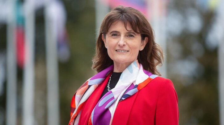 Head shot of French meteorologist Dr. Florence Rabier, wearing a red jacket, a white and purple scarf and black shirt.